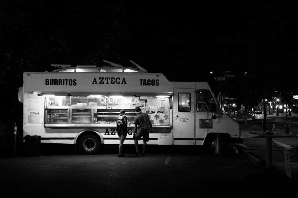 Grayscale Photograph of Two People Standing in Front of Food Truck