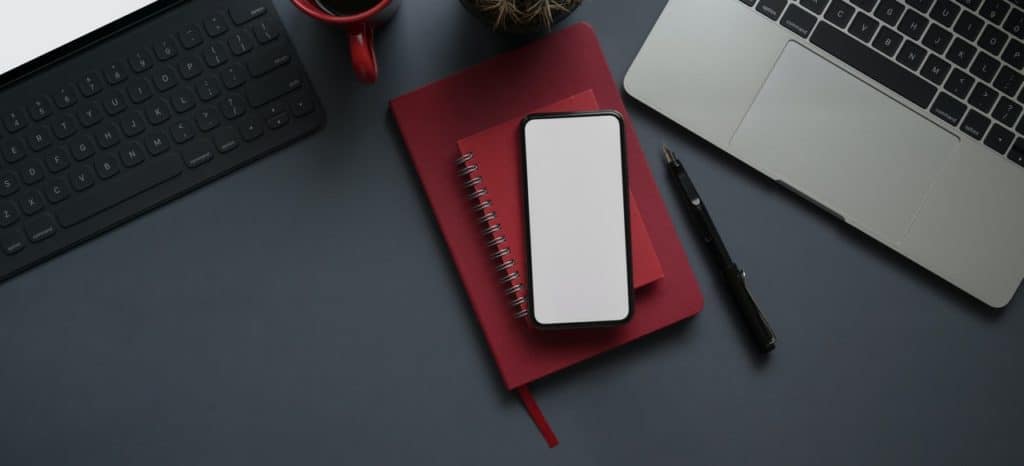 Red Notebook and Smartphone Beside Computer Laptop