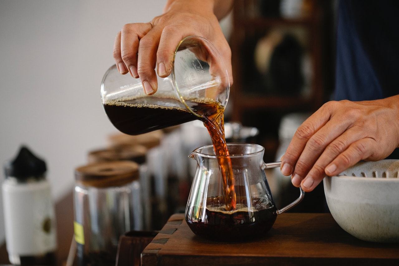 Unrecognizable male barista pouring freshly brewed coffee into glass pot